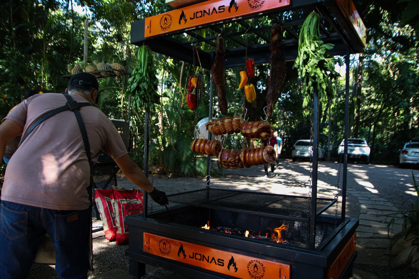 Carrinho de brasa JONAS com carnes penduradas e fogo aceso